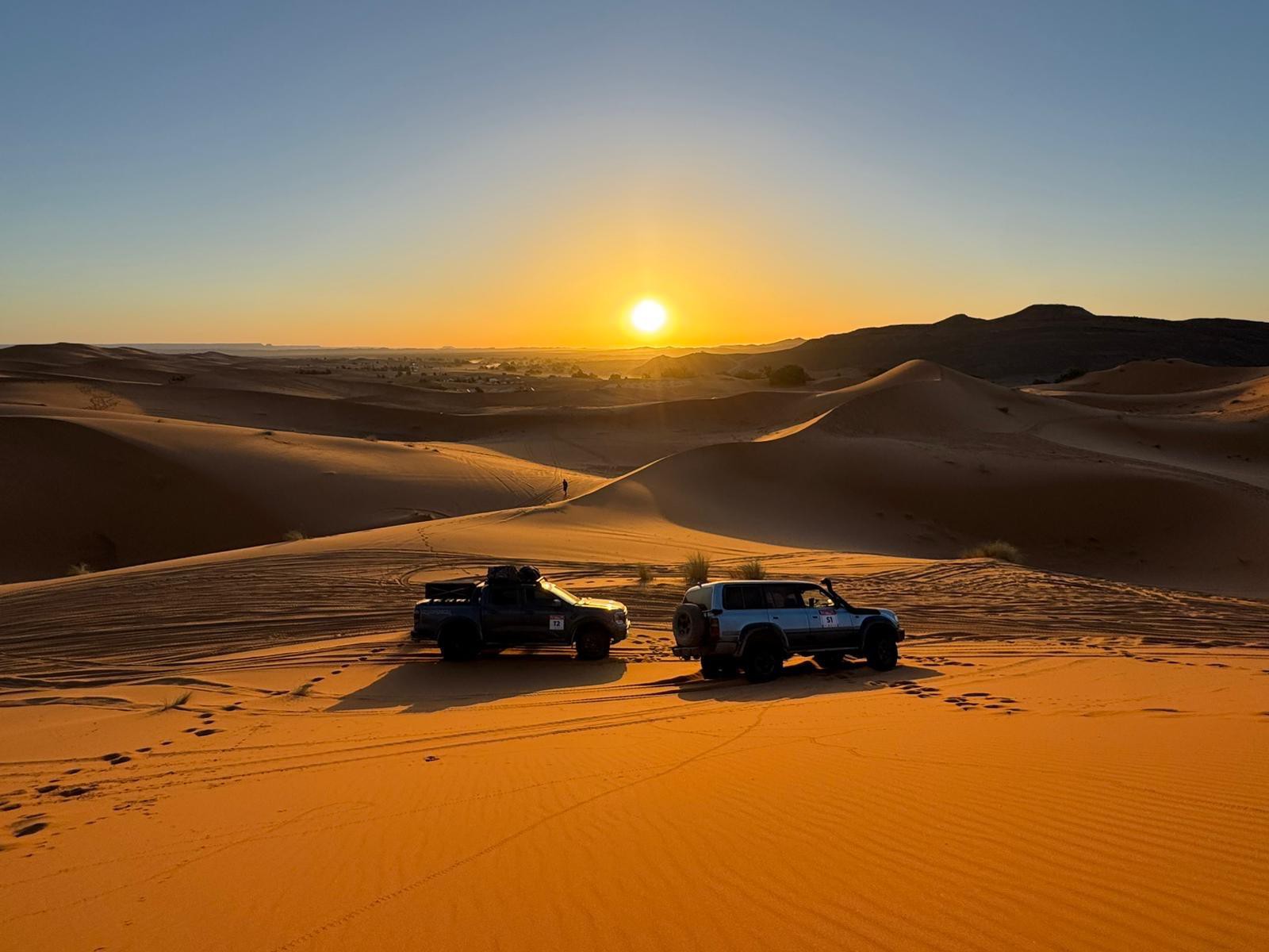 Photo de deux 4x4 dans le désert sous un coucher de soleil prise durant le rallye rose des sables 2025